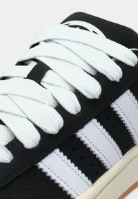 Svart-hvitt joggesko med teksturert skinn, hvite flate lisser og en gummisåle, med tre svarte striper og perforeringer på siden.