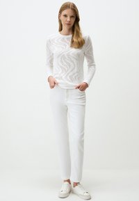 Witte lange mouwen top met opengebreid zigzagpatroon, gecombineerd met witte rechte broek en witte sneakers, wat een monochromatische look creëert.