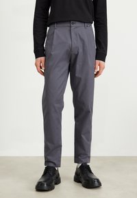 Grey tailored pants with a smooth texture, featuring a front crease, button closure, and side pockets, paired with black shoes.