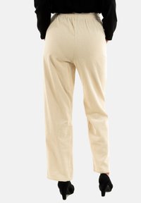 Beige ribfluweel broek met een elastische tailleband, strak ontwerp en subtiele ribbelstructuur. Draagt het met zwarte hakken.