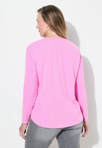 Maglietta a maniche lunghe in tessuto fucsia, con scollo rotondo e superficie liscia, fotografata da dietro.