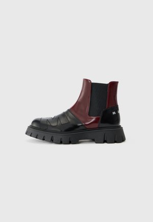 Svarta och vinröda Chelsea-boots med kraftiga sulor, utrustade med elastiska sidopaneler och strukturerad läderdetalj.