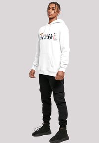 Sudadera blanca con bolsillo frontal tipo canguro, estampado gráfico de figuras, puños acanalados, combinada con pantalones cargo negros y zapatillas negras.