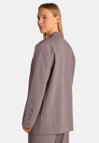 Blazer gris a rayas con detalles metálicos, ajuste entallado, cuello con muescas y detalle de puño abotonado; textura de tela suave.