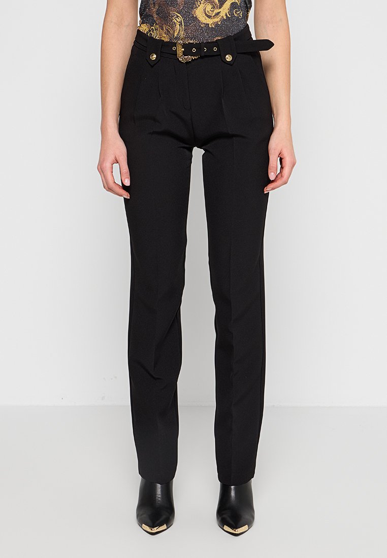Pantalon noir ajusté à taille haute, avec des plis, une ceinture sash ornée de détails en métal doré. Tissu lisse avec une coupe droite.