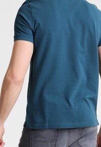 T-shirt en coton à manches courtes de couleur bleu canard, avec un col rond, présentant une texture lisse et une coupe droite à l'ourlet.