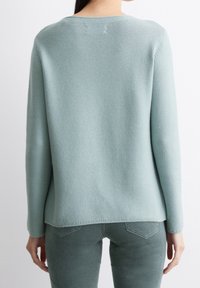 Světle modrý pletený svetr s texturovaným vzorem, dlouhými rukávy a kulatým výstřihem, s lemem, který je mírně delší vzadu.