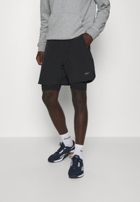 Černé sportovní šortky s vnitřní podšívkou, spárované s navy teniskami a bílými ponožkami Reebok. Šedá mikina s kapucí. Jednoduché designové prvky.