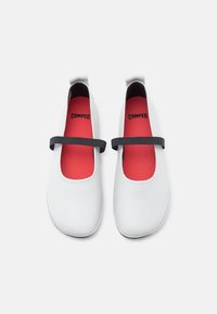 Λευκά δερμάτινα παπούτσια με στρογγυλεμένη μύτη, διαθέτουν μαύρο ελαστικό λουράκι και κόκκινο εσωτερικό πέλμα. Σχεδιασμός με επίπεδη σόλα και ελάχιστες ραφές.