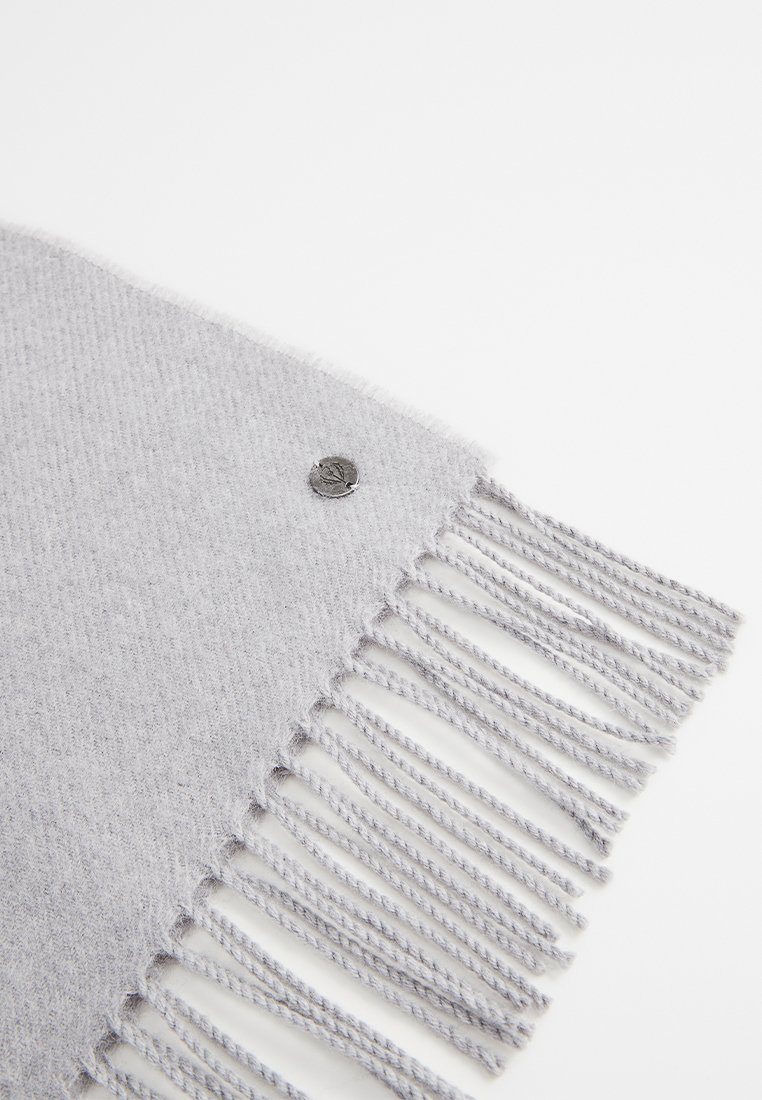 Hellgrauer Schal aus weichem Material, mit Fransenbesatz und einem kleinen silbernen Emblem. Schlichtes Design mit glatter Textur.
