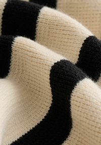 Strickstoff mit kräftigen creamfarbenen und schwarzen Streifen, der eine weiche Textur und ein leicht flauschiges Aussehen aufweist, mit dicken, abwechselnd angeordneten Bändern.