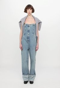 Denim trebušaste hlače svetlo modre barve z visokim pasom, širokimi nogami, sprednjim žepom in zadrgo. Slojevito oblečene s sivo kratko majico.