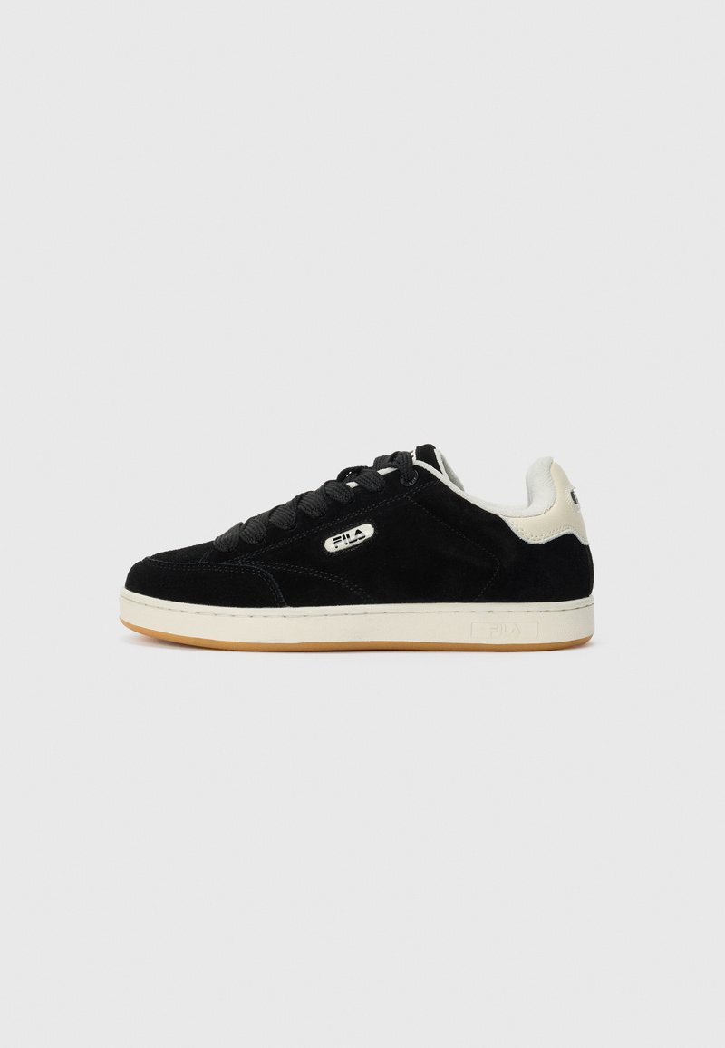 Zapatilla FILA negra y blanca de caña baja con diseño de cordones, suela beige y logo en el lateral y en el talón, mostrada de perfil sobre fondo blanco.