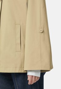 Jasbeżowa, lekka kurtka z dużymi dzwonowymi rękawami, z boczną kieszenią i zapięciem na guzik przy mankiecie. Gładka tekstura tkaniny.