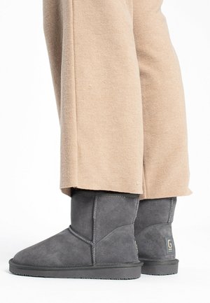 Botines de ante gris con punta redondeada, suela de goma plana y costuras sutiles. Combinados con pantalones de pierna ancha beige.