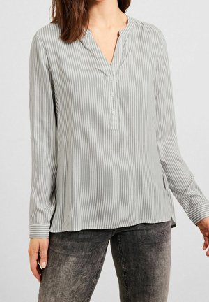 Woman wearing a light gray vertically striped long-sleeve blouse with a partial button placket and faded black jeans.