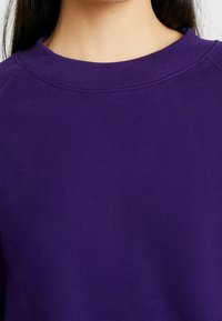 Lila Sweatshirt aus strukturiertem Stoff, mit geripptem Rundhalsausschnitt und lockerer Passform. Sichtbare Nähte am Kragen.