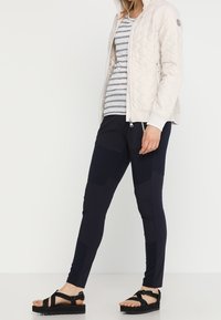 Chaqueta acolchada beige claro, leggings estampados en azul marino, camisa gris rayada, sandalias negras con tiras, detalles en tono carne. Texturas suaves.