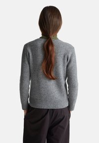 Šedý vlněný svetr s vroubkovaným lemem a manžetami, jednoduchým kulatým výstřihem a volným střihem. Nositý přes zelený oděv.