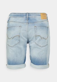 Pantalones cortos de mezclilla azul claro con efecto desgastado, puños doblados y dos bolsillos traseros con detalles de costura curva. Etiqueta beige en la cintura.