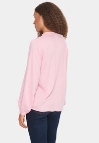 Blusa de manga larga color rosa claro con tejido texturizado, escote redondo y puños fruncidos, combinada con jeans azul oscuro.