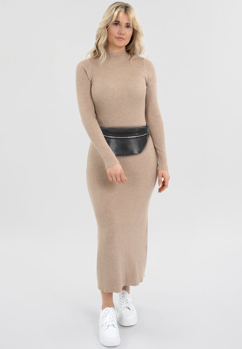 Langes, geripptes Kleid in hellem Beige mit einer figurbetonten Silhouette. Kombiniert mit einer schwarzen Bauchtasche und weißen Plateausneakern.