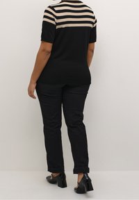 Musta lyhythihainen neule, jossa raidallinen beige yläosa, yhdistetty mustiin housuihin ja mustiin korkokenkiin. Sileä pinta, rento muotoilu.