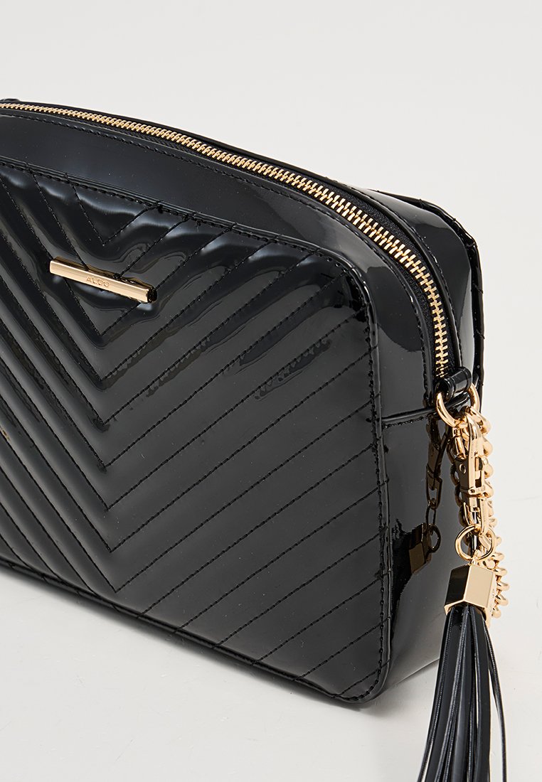 Clutch en cuir verni noir avec un motif en chevrons matelassé, quincaillerie dorée et un accent à franges. Dispose d'une fermeture zippée sur le dessus.