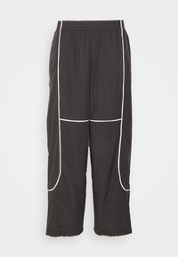 Musta, löysästi istuvat housut, joissa valkoiset reunalistat saumoissa ja vetoketjulliset taskut. Kuminauhavyötärö ja nilkoissa kerätyt resorit.