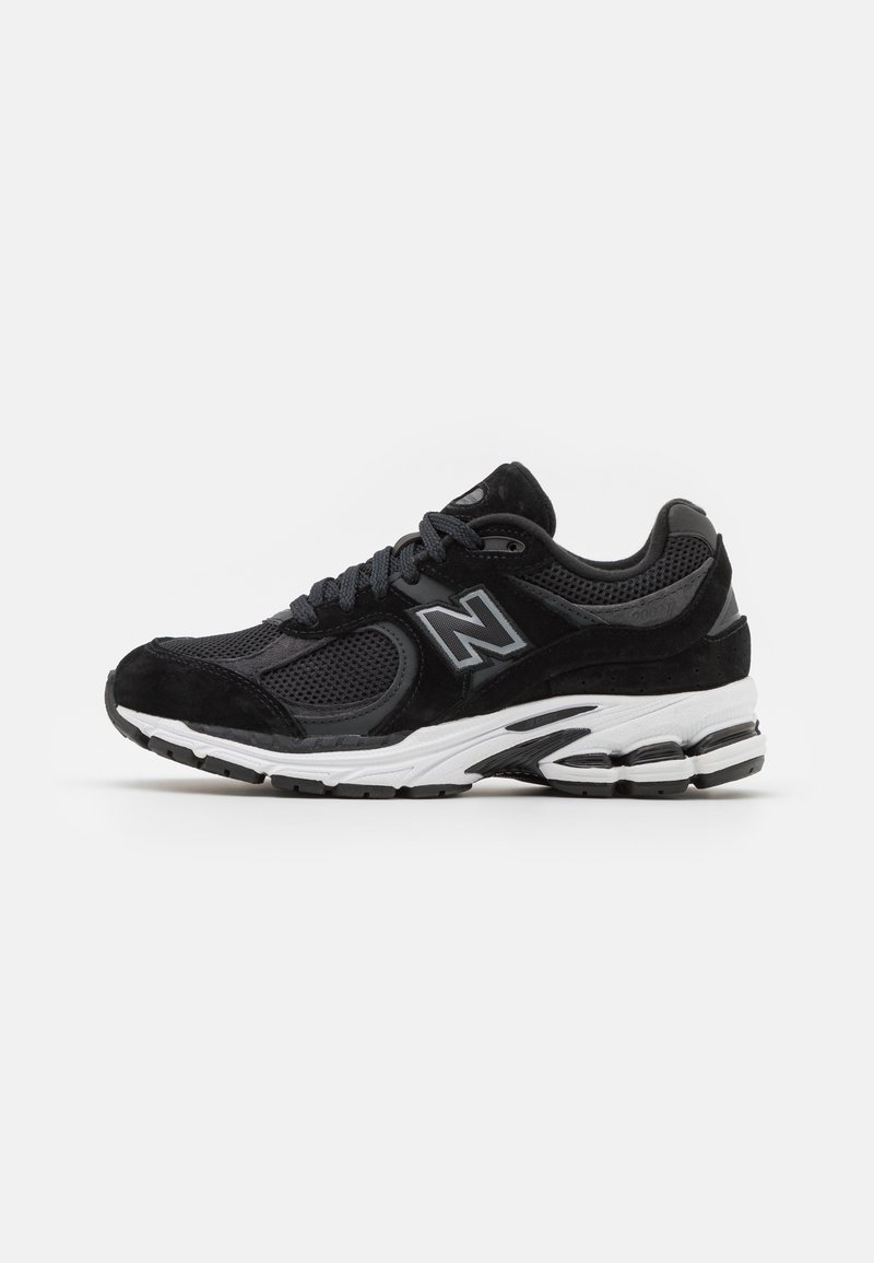 Chaussure de running New Balance noire et grise avec une tige en mesh et en suède, semelle blanche amortissante et design à lacets sur fond blanc.