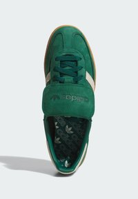 Green suede sneakers featuring a textured upper, white stripes, and a velcro strap. Gum sole; interior displays repeated adidas logo pattern.