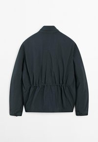 Giacca leggera e scura con vita arricciata, colletto piatto e maniche lunghe. Texture liscia senza modelli o accessori visibili.