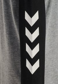 Graues T-Shirt mit schwarzem Ärmel, das mit drei weißen Chevronstreifen verziert ist. Weicher Baumwollstoff, klassischer Rundhalsausschnitt, lässiger Schnitt.