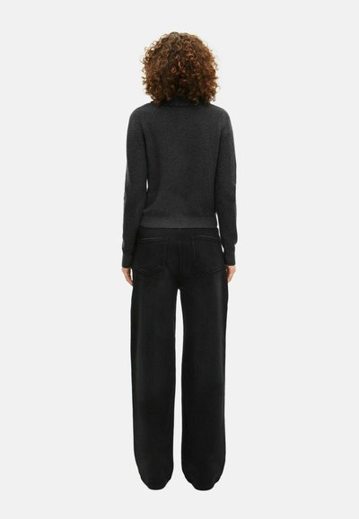 Zwarte, loszittende broek met zakken, gecombineerd met een donkere, strakke trui met een golvende halslijn en geribde manchetten.