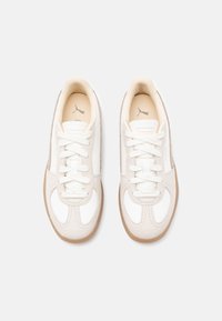 Scarpe da ginnastica bianche e beige con tomaia in pelle liscia, dettagli in camoscio, punta rotonda e lacci piatti; dotate di suola in gomma texturizzata.