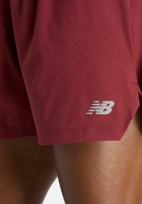 Pantaloncini sportivi color marsala in tessuto traspirante, con un piccolo logo bianco New Balance e una vestibilità comoda con texture forata.