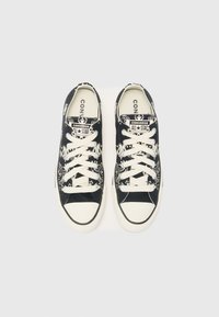 Črne platnene teniske z belim vzorcem, belimi vezalkami in gumijastim pokrovčkom za prste. Na jeziku je logotip "Converse All Star", okrogla oblika prstov.