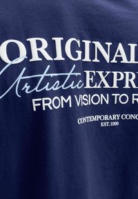 Tissu bleu marine avec texte blanc et bleu clair indiquant « ORIGINAL Artistic EXPRESS FROM VISION TO REALITY CONTEMPORARY CONCEPT EST. 1990. »