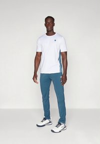 Vit kortärmad skjorta med turkosa detaljer, kombinerad med tealfärgade byxor och vita sneakers. Atletisk passform med en diskret logga på skjortan.