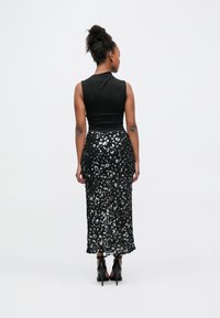 Mustast võrguselt õlgadeta topp, mis on keha järgi lõigatud, kombineeritud pika musta seelikuga, mis on kaunistatud hõbedaste lillekujuliste litritega, detailse äärega ja kõrgete kontsadega.