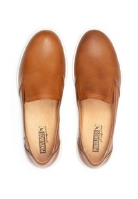 Zapatos marrones sin cordones con una parte superior de cuero texturizado, acentuados por una suela de goma blanca. El interior cuenta con un forro de color claro con la marca.