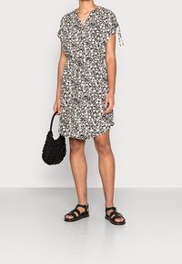 Abito floreale bianco e nero a maniche corte con vita regolabile e orlo a lunghezza ginocchio; abbinato a sandali neri e una borsa nera testurizzata.