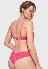 Conjunto de bikini rosa con tirantes finos y cierre en la parte posterior. Presenta detalles fruncidos en la parte superior y acentos arrugados en la parte inferior del bikini.