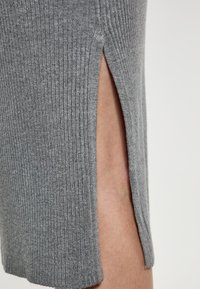Šedá žebrovaná tkanina s bočním rozparkem, která ukazuje hladkou texturu a přiléhavý design. Důraz na tvar a přidání dimenze.