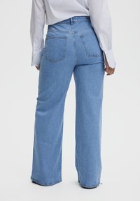 Široke jeans hlače iz modrega denima s sproščenim fitom, z zadnjimi žepi in visokim pasom. Tkanina ima gladko teksturo.