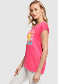 Lyserød bomulds t-shirt med korte ærmer, prydet med farverig grafik tekst og lyn design, kombineret med lyse bukser.