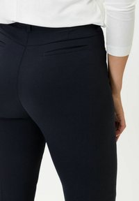 Pantaloni scuri in navy realizzati in un tessuto morbido, con un design aderente, due tasche posteriori e vita a media altezza.