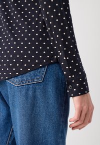 Mørkeblå prikkete skjorte med lange ermer og knappesøm, kombinert med blå denimbukser med detalj på baklommen.