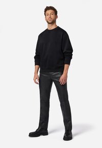 Sort fleece sweatshirt med lange ærmer, parret med tætsiddende sorte læderbukser og sorte snørebåndsstøvler, stående på en hvid baggrund.