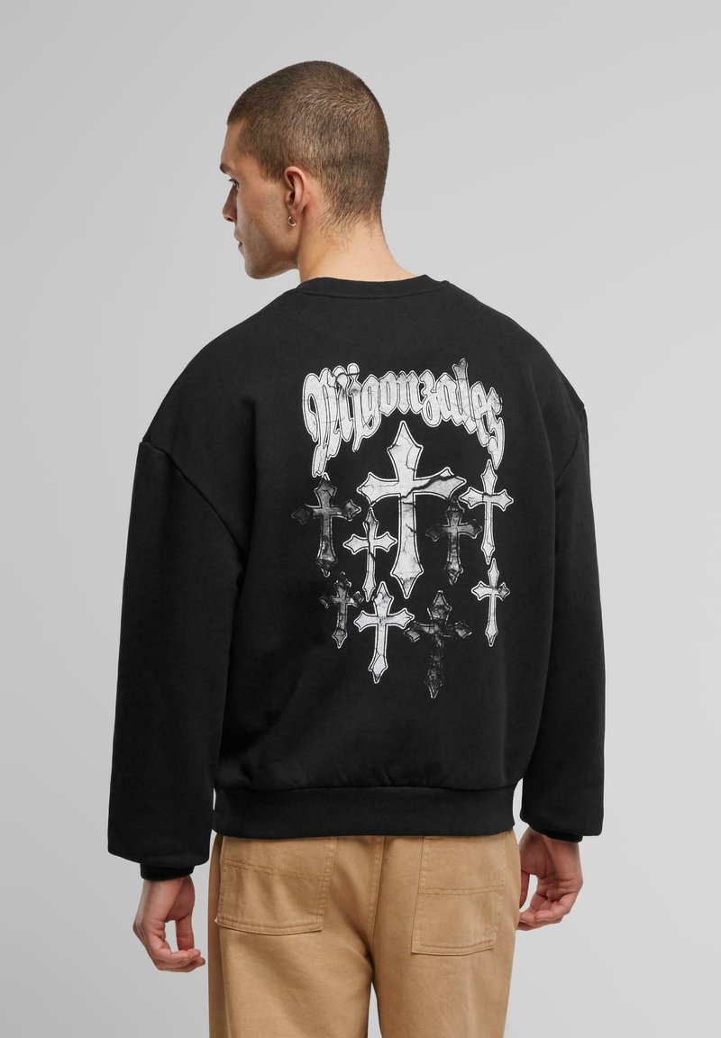 Zwarte fleece sweatshirt met een grote grafische afbeelding van verschillende kruisen en tekst op de achterkant, met een ronde hals en drop shoulders.